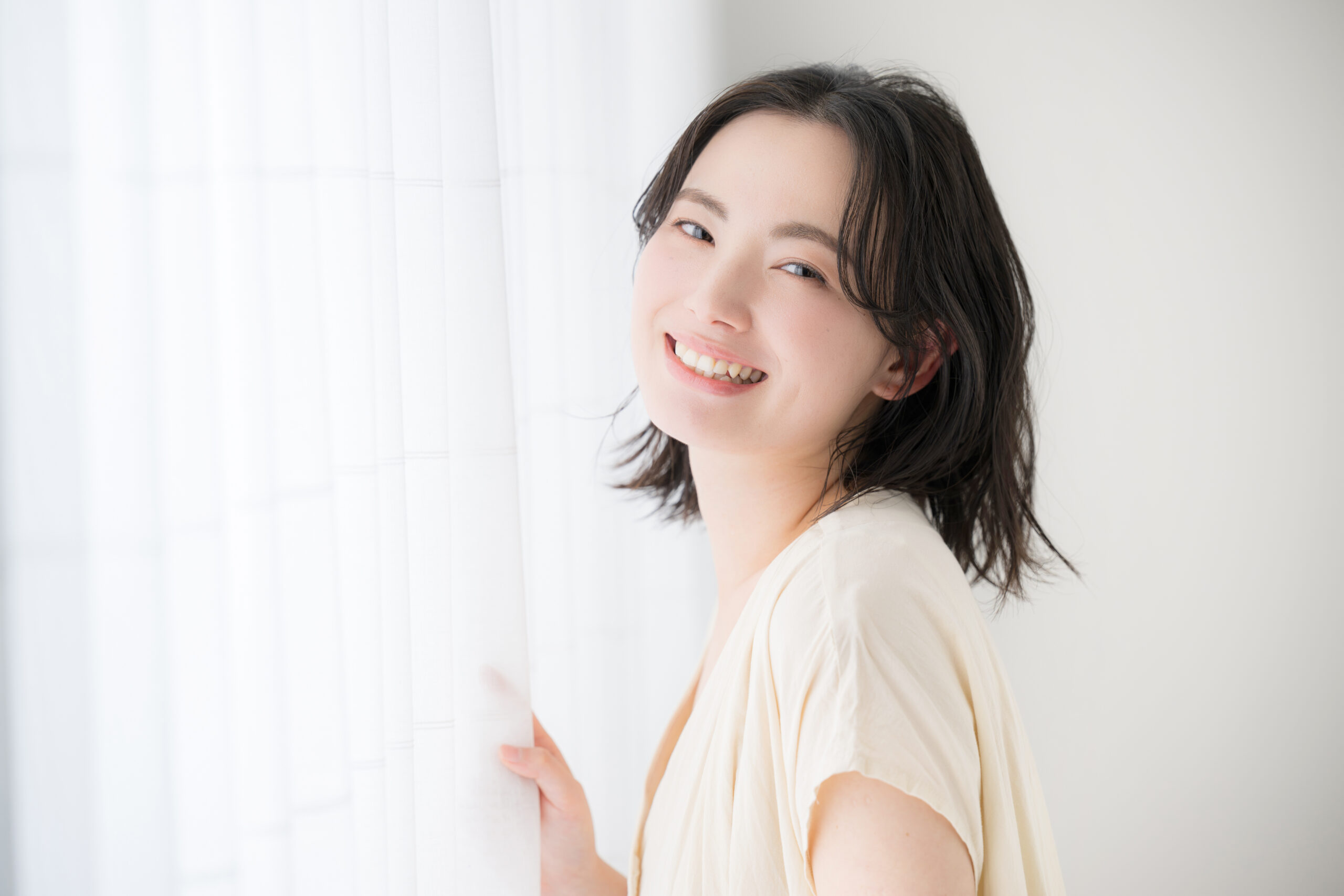 カーテンを掴みこちらを見て微笑む女性