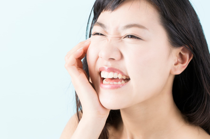 歯の激痛で頬を押さえ顔をしかめる女性