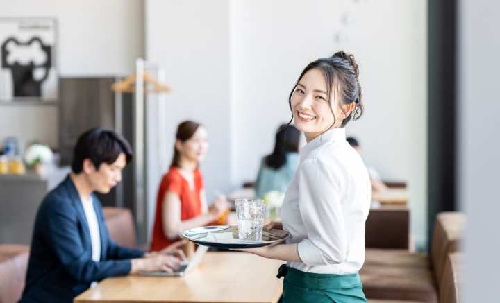 ホームホワイトニングをした白い歯に満足して笑顔で働くカフェ店員の女性