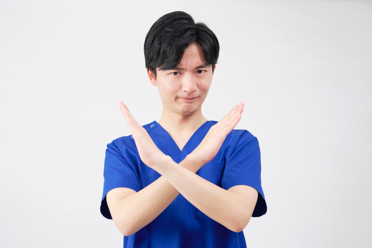 両手でバツマークをする歯科医